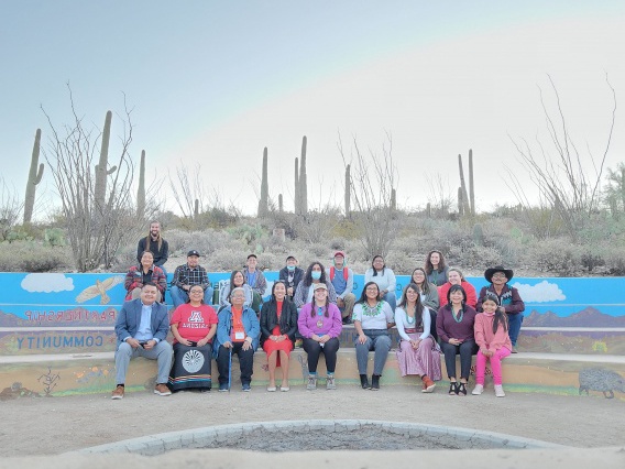 ITEP group photo of several men and women sitting on a bench under a hazy sky with cactus in the background